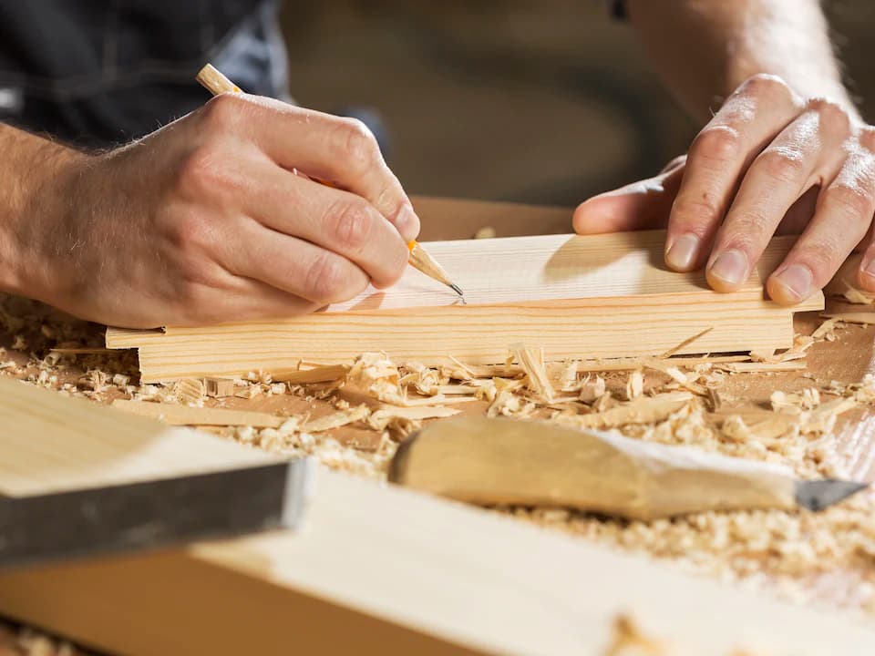 Un artesano traza una marca a lápiz en una tabla de madera.