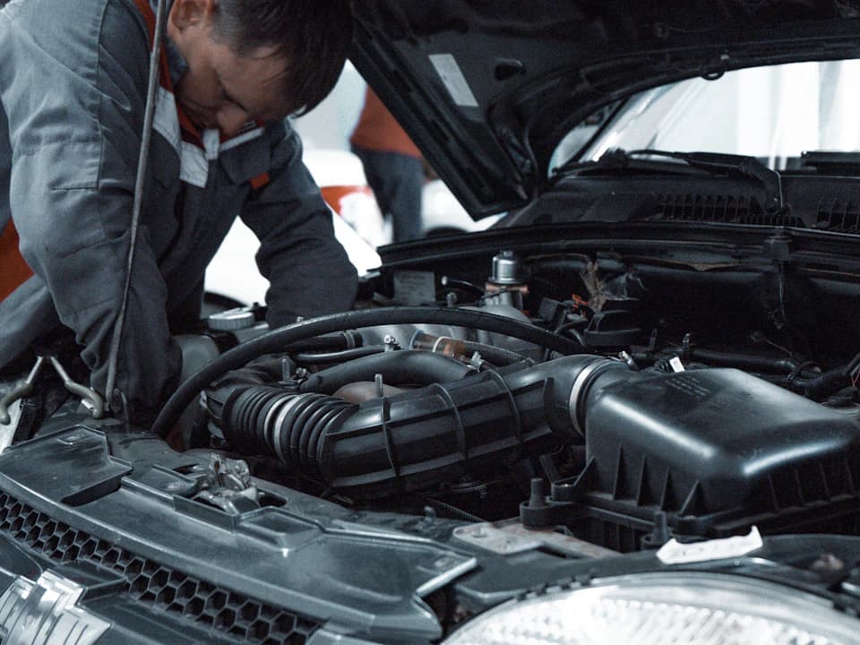 Un mecánico con ropa de trabajo inspecciona el motor de un vehículo.