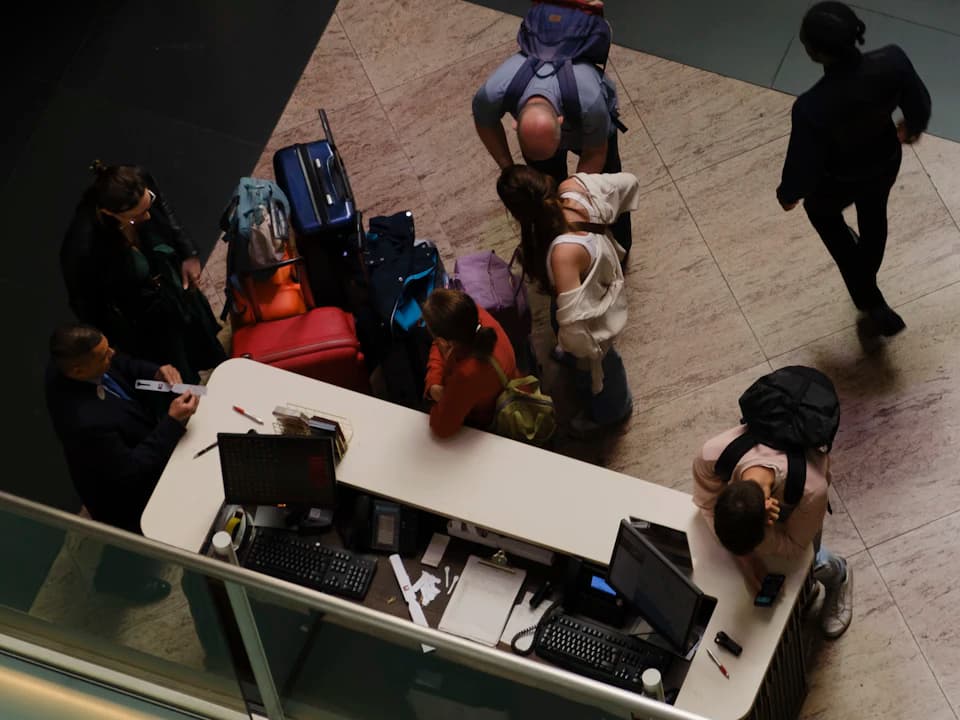 Unos viajeros con su equipaje en la recepción de un hotel, vistos desde arriba.