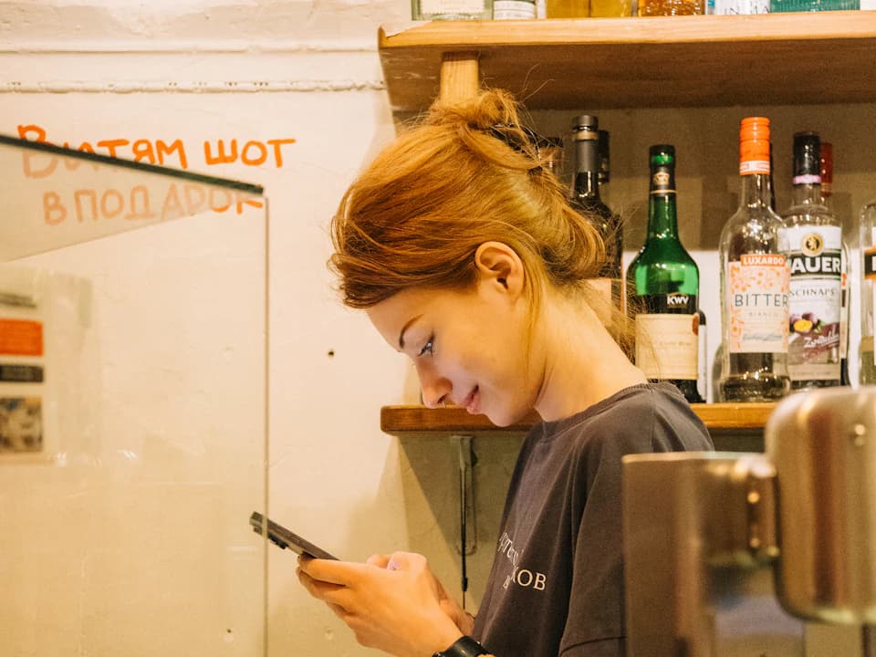 Una camarera consulta su teléfono detrás de la barra de un restaurante.